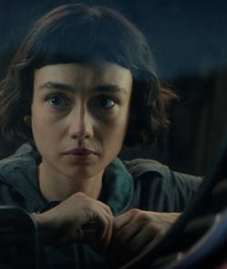 Sydney Chandler as Wendy, the human-synthetic hybrid, looking through a window in Alien: Earth.